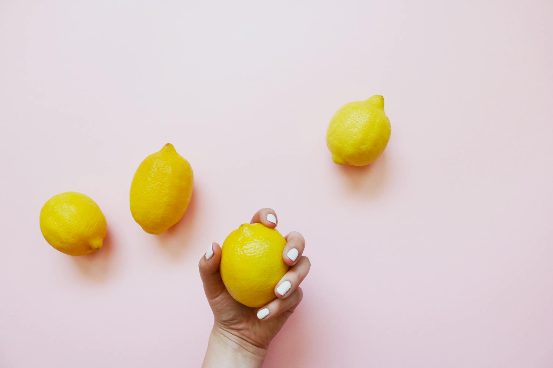 A hand holding a lemon on a soft pink background, symbolizing renewed sensation and vitality.