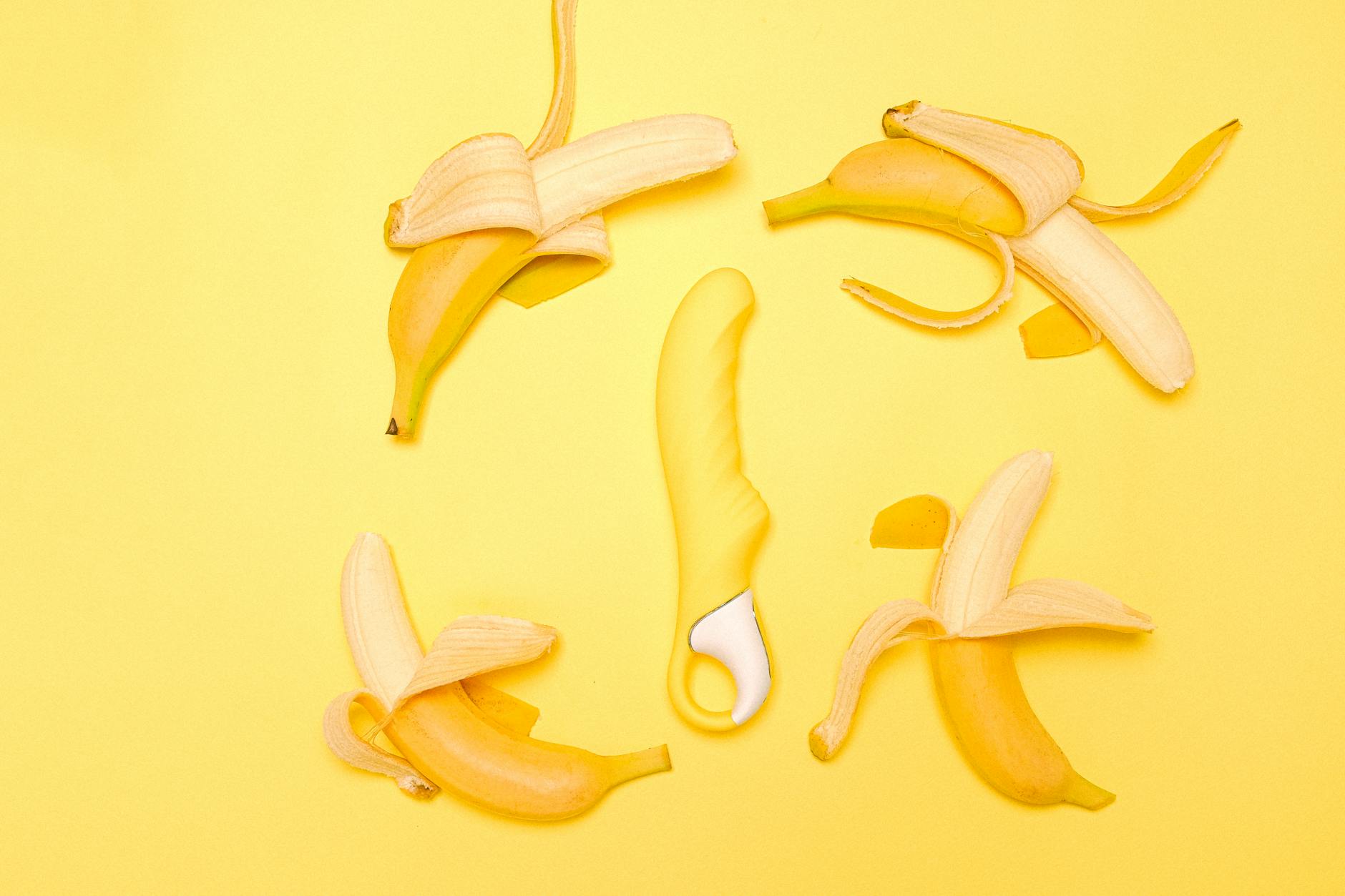 Yellow silicone lemon vibrator surrounded by fresh lemons on a bright yellow background.