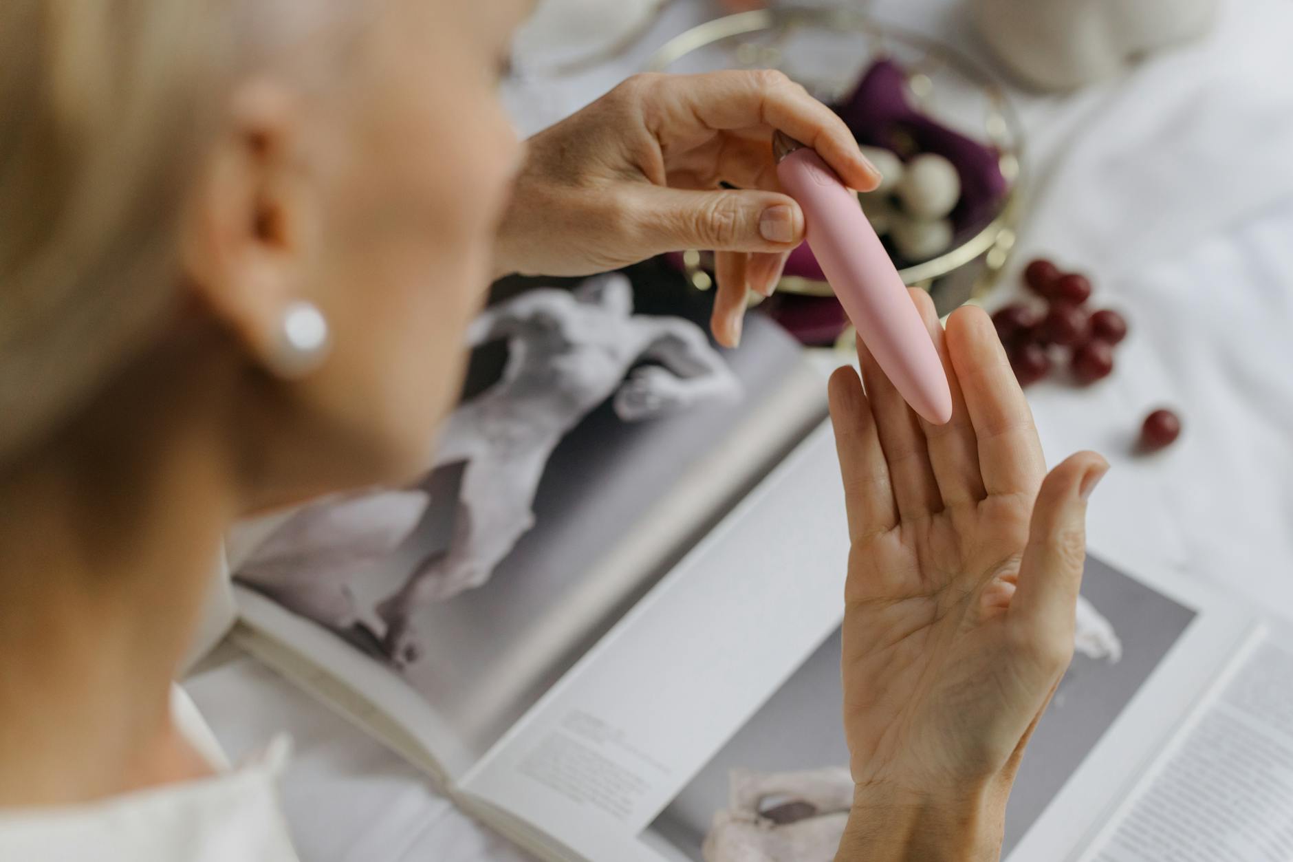 Woman holding a pink vibrator with art books in background, representing intimate self-exploration and personal pleasure