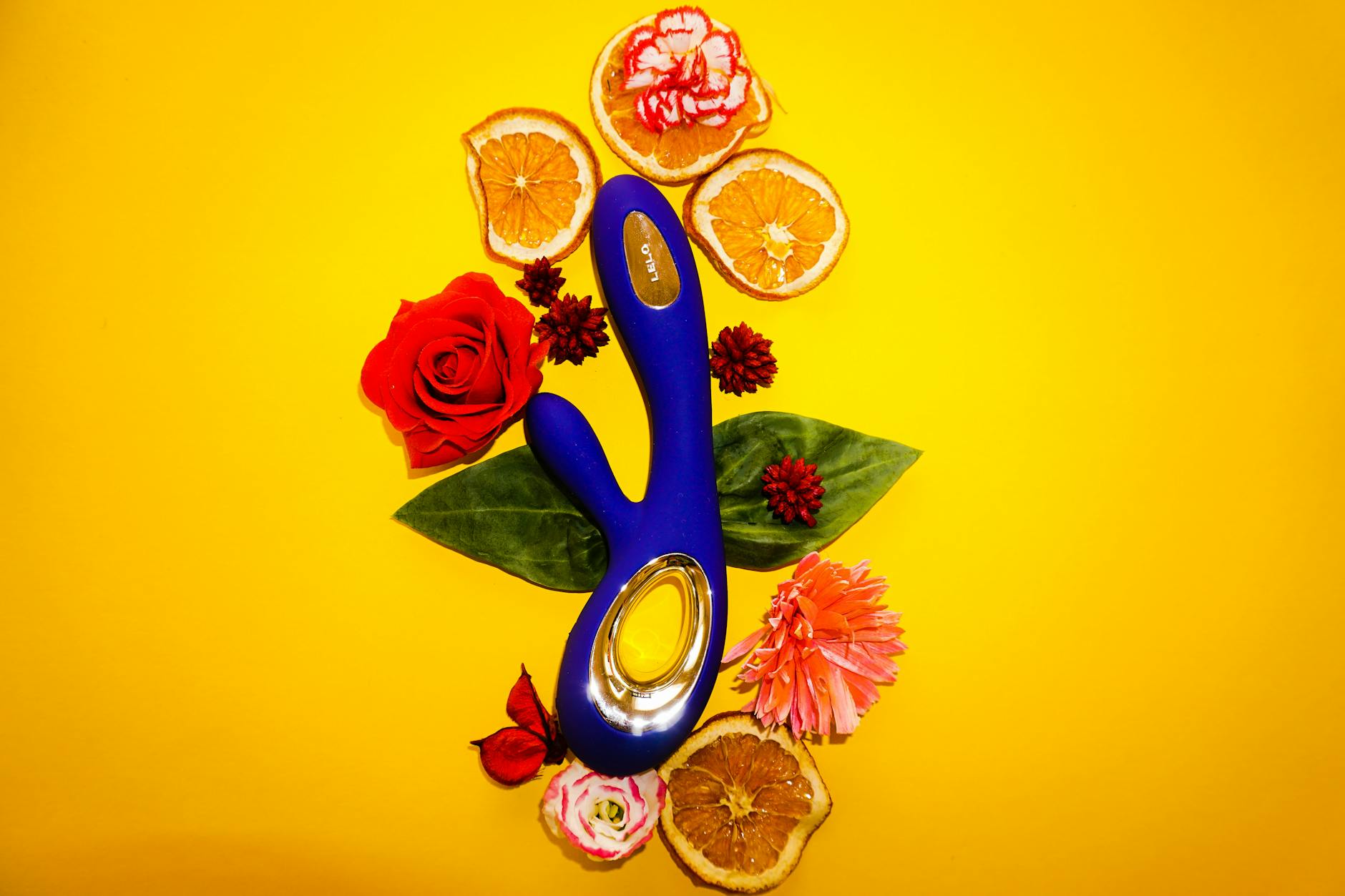Lemon vibrator surrounded by flowers and citrus on bright yellow background